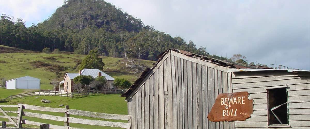 A rural landscape with a wooden barn, a warning sign, and a mountain in the background.