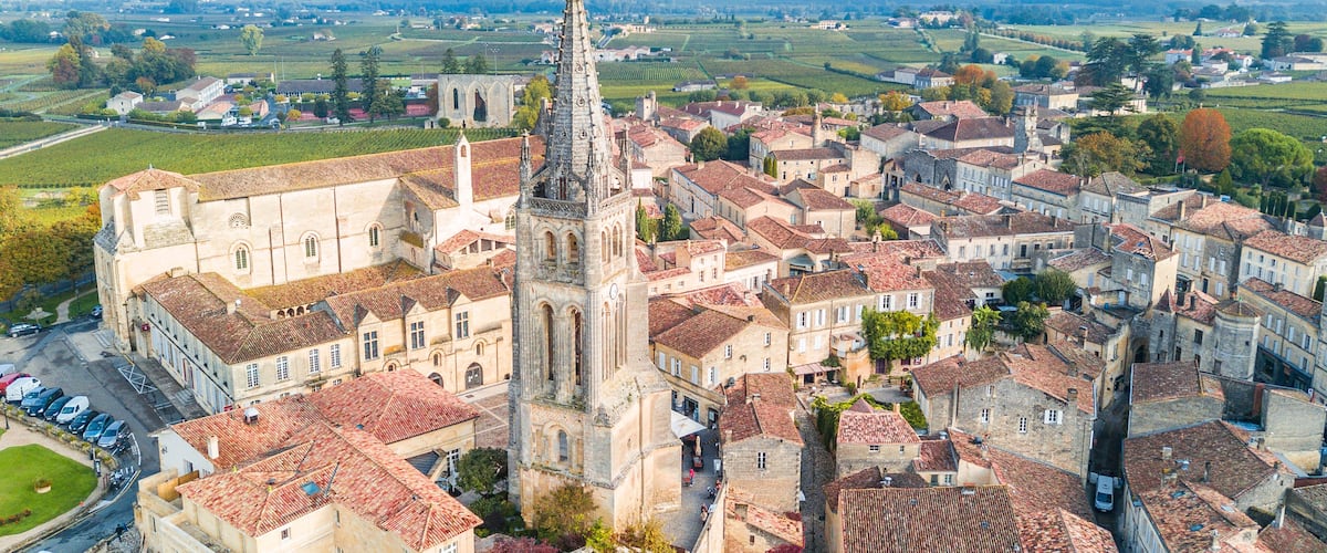 A historic town with a prominent church featuring a tall spire, surrounded by traditional buildings and vineyards in the background.
