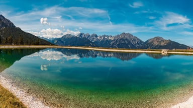 A clear lake reflecting mountains, a gravel path, and a wooden fence.