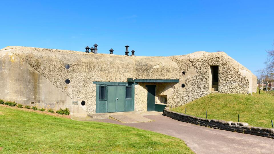 A stone building with a green door and windows, surrounded by a grassy area and a stone wall.