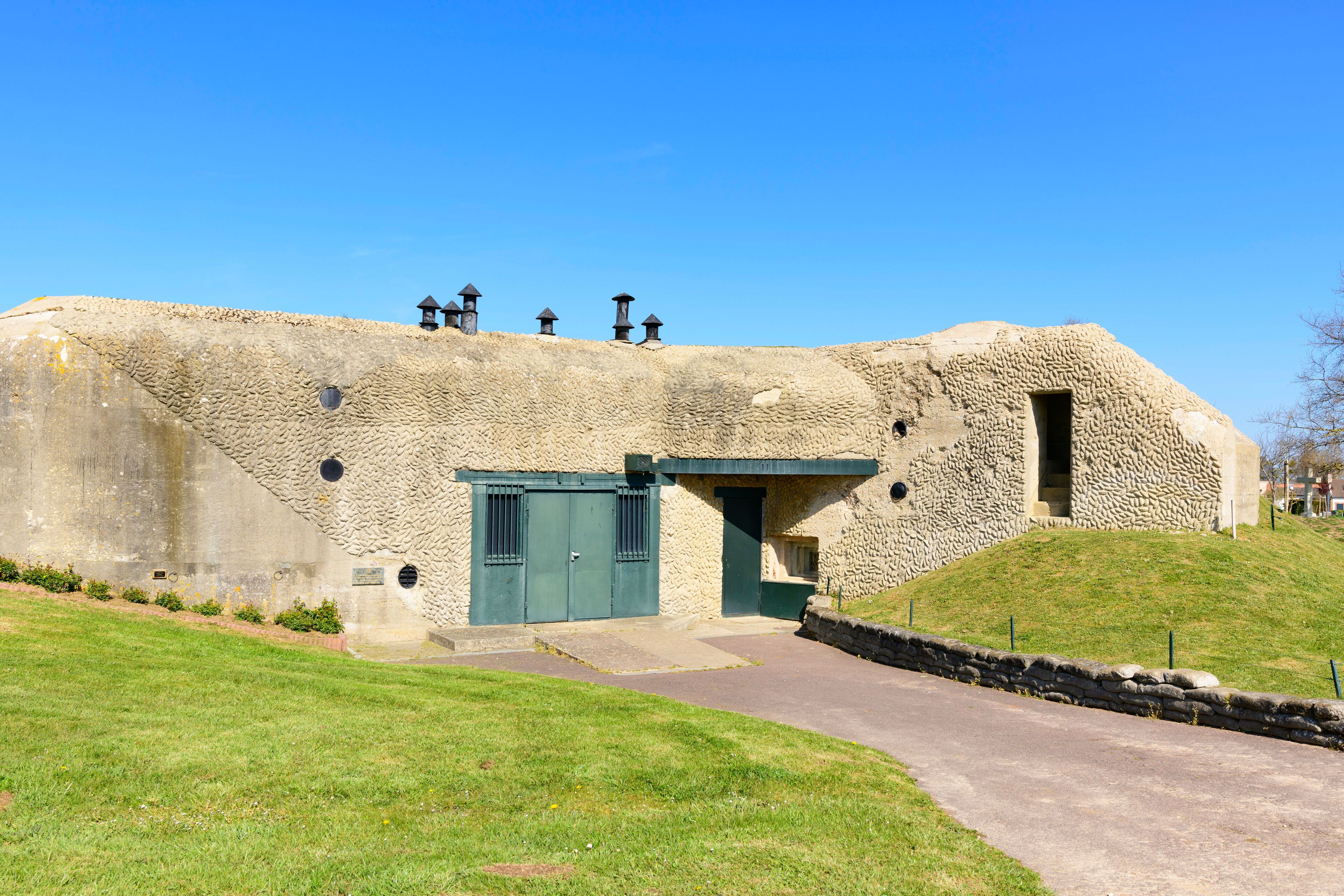 A stone building with a green door and windows, surrounded by a grassy area and a stone wall.