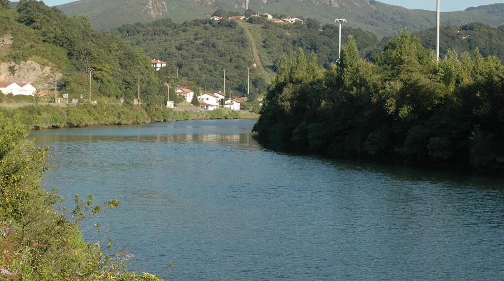 La Bidassoa, vue vers l'amont depuis la D811 près de la redoute Louis XIV. La commune de Biriatou est à gauche (en rive droite) de la Bidassoa (le village lui-même est derrière nous) ; l'Espagne est à droite (en rive gauche). Le hameau d'Aruntz et son pylône sont sur la première hauteur à mi-plan ; ce qui semble être un chemin menant tout droit vers ce sommet, est le passage de lignes à haute tension. La barre rocheuse du Lumaberde est légèrement sur sa gauche (derrière ce sommet), et plus loin derrière le mont du Calvaire (277 m alt.). Le pont de Bénobie, sur le territoire d'Urrugne, est à environ 580 m derrière nous. Le pont de l'autoroute A63 est devant nous, juste après le coude de la rivière.