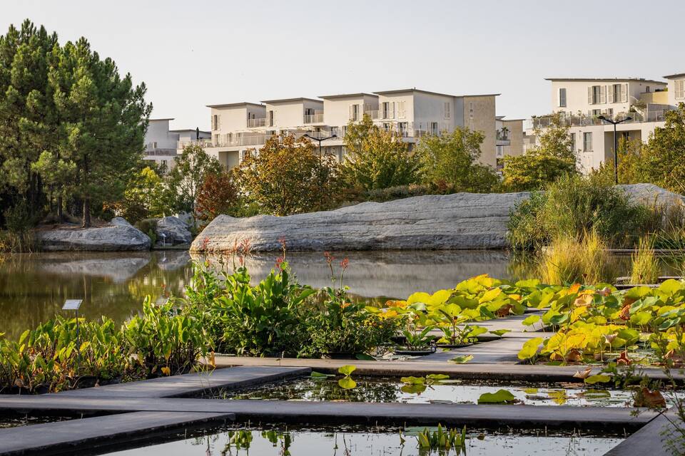 Un lago tranquilo con edificios modernos, abundante vegetación y una superficie acuática serena.