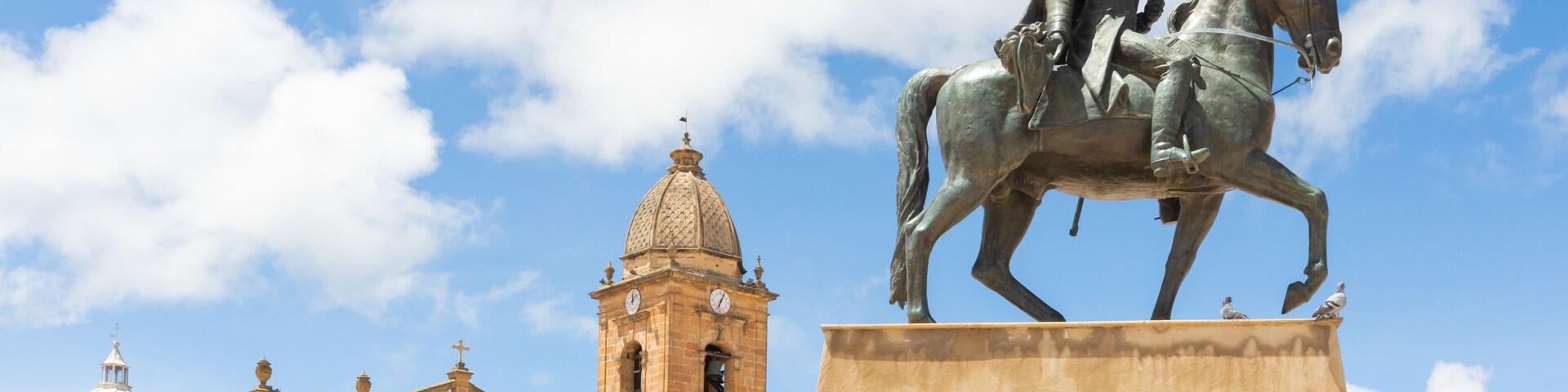 Una estatua de un hombre a caballo frente a un edificio histórico con una torre de reloj.