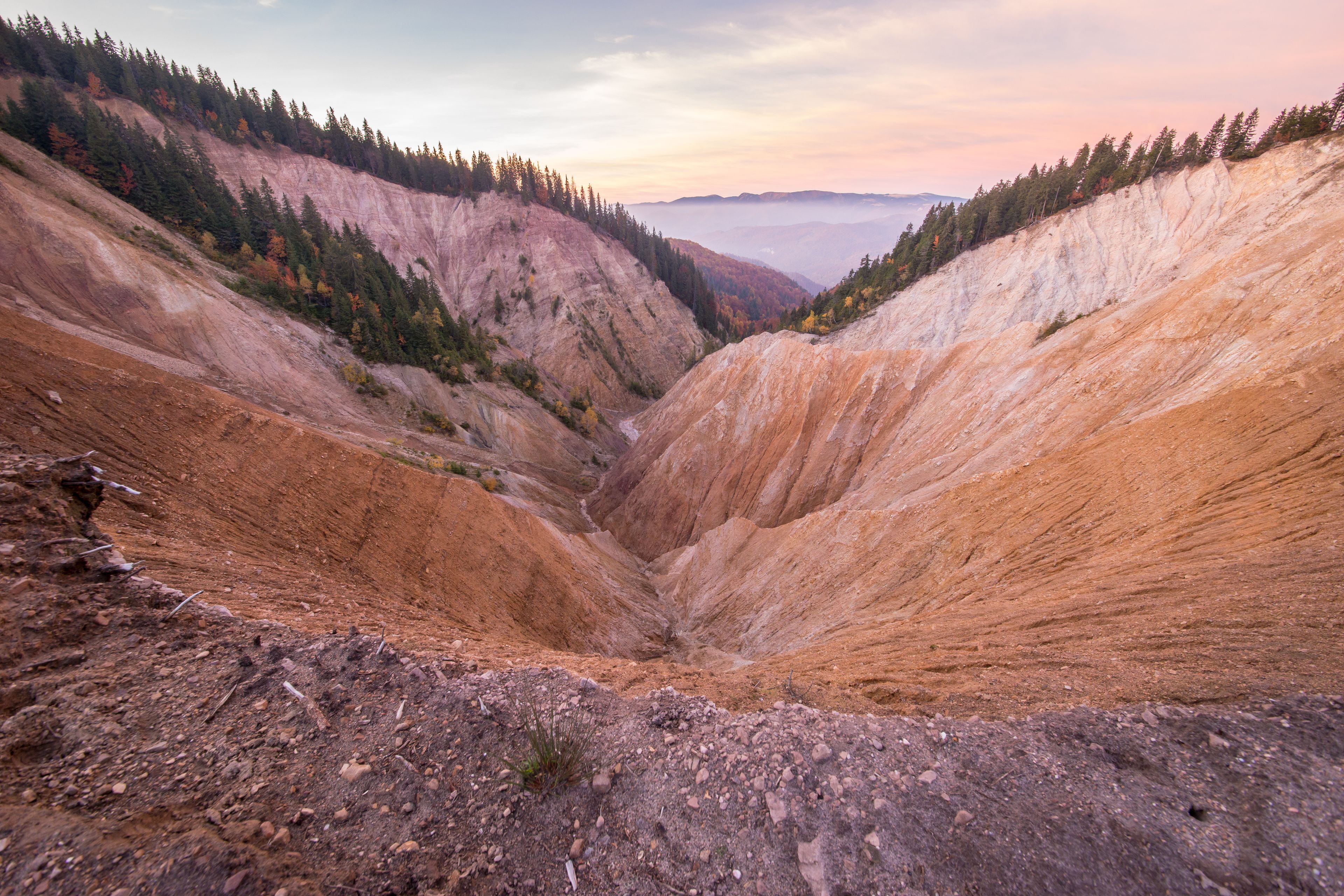 A canyon with steep, reddish-brown walls and a valley floor.