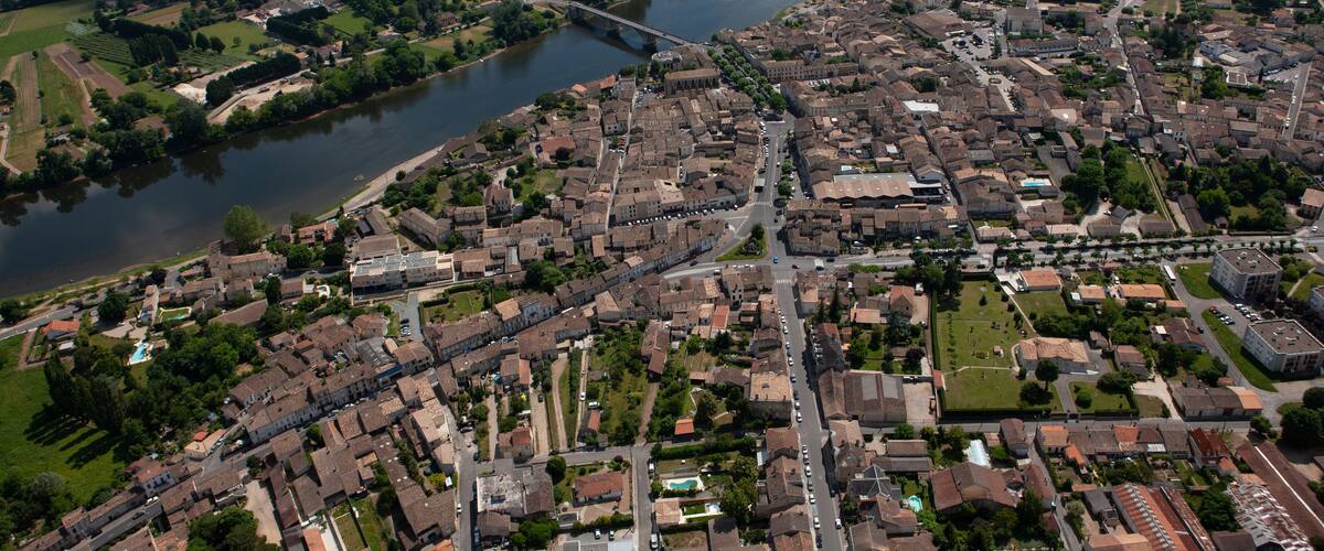 An aerial view of a town with a river, a bridge, and surrounding fields.