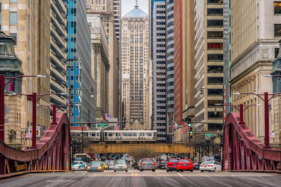 Una calle urbana concurrida con un paso de tren, edificios altos y un tranvía.