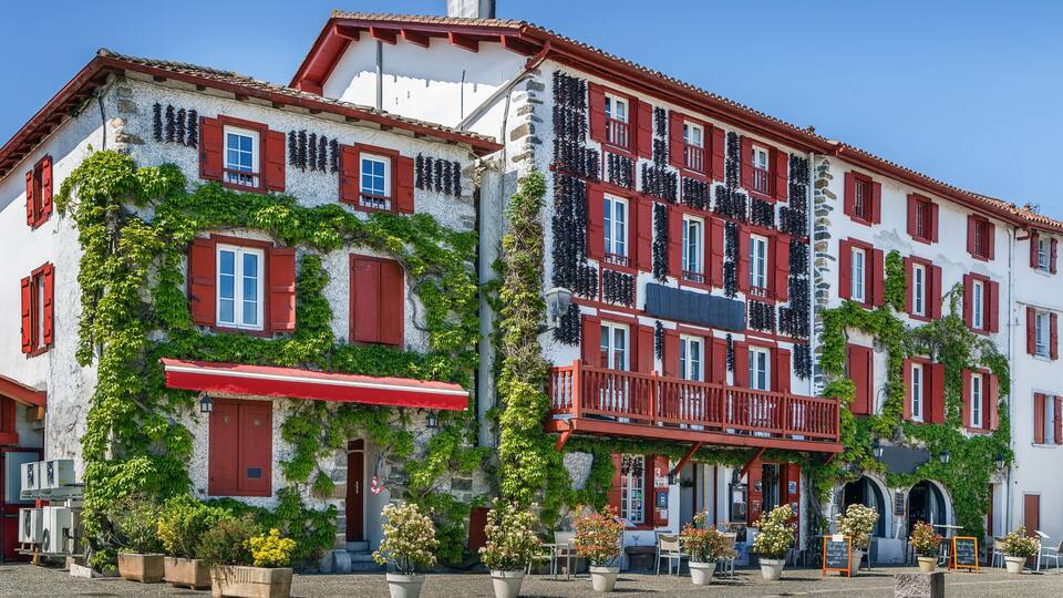 A historic building with red shutters and white walls, covered in green vines, and a red awning.
