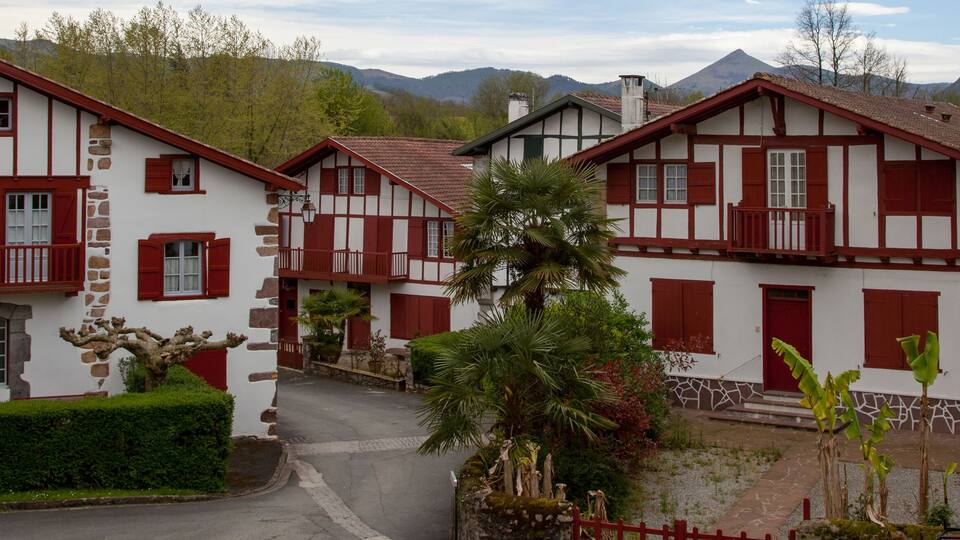 A traditional European village with white and red timber-framed houses, surrounded by lush greenery and mountains.