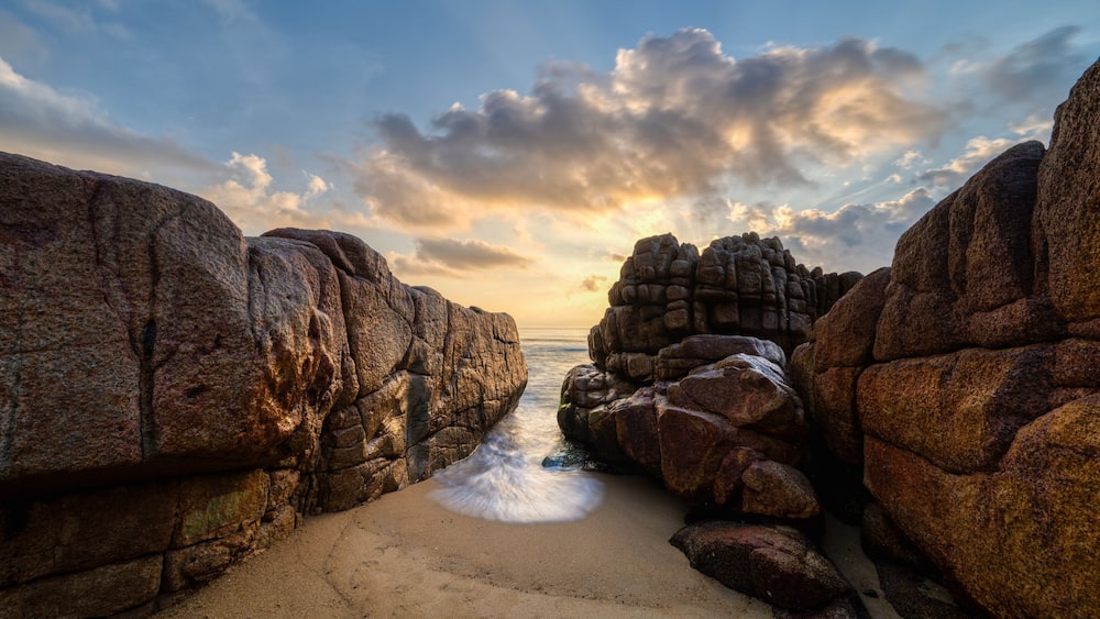 Long exposure photo of waves and rocks at sunrise.