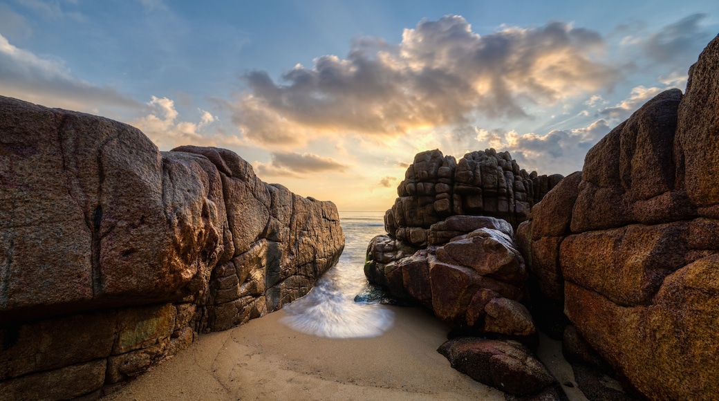 Long exposure photo of waves and rocks at sunrise.
