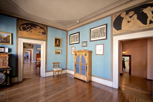 Une pièce aux murs bleus, au plancher en bois, et ornée de divers tableaux et meubles encadrés.