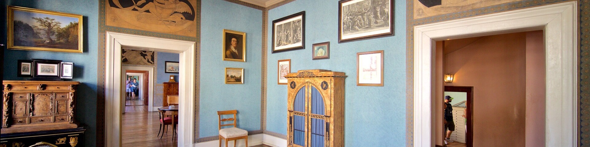 Quarto com paredes azuis, piso de madeira e diversos quadros emoldurados e mobiliário.