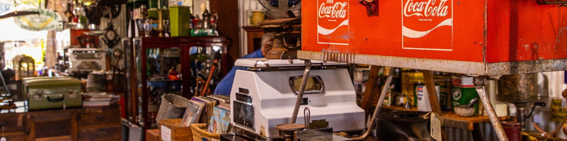 Una tienda de antigüedades abarrotada con objetos antiguos y una máquina expendedora de Coca-Cola.