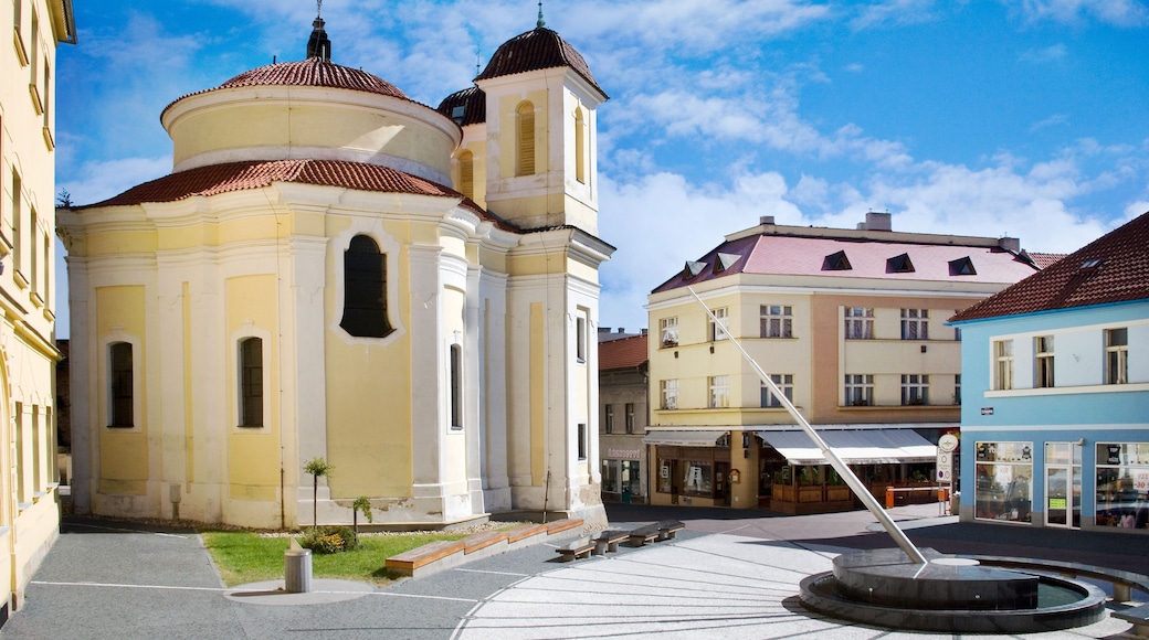 Una iglesia histórica con un campanario, una fuente y edificios circundantes.