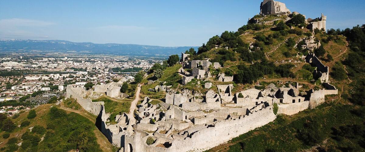 A historic castle atop a hill with ruins below, overlooking a cityscape.