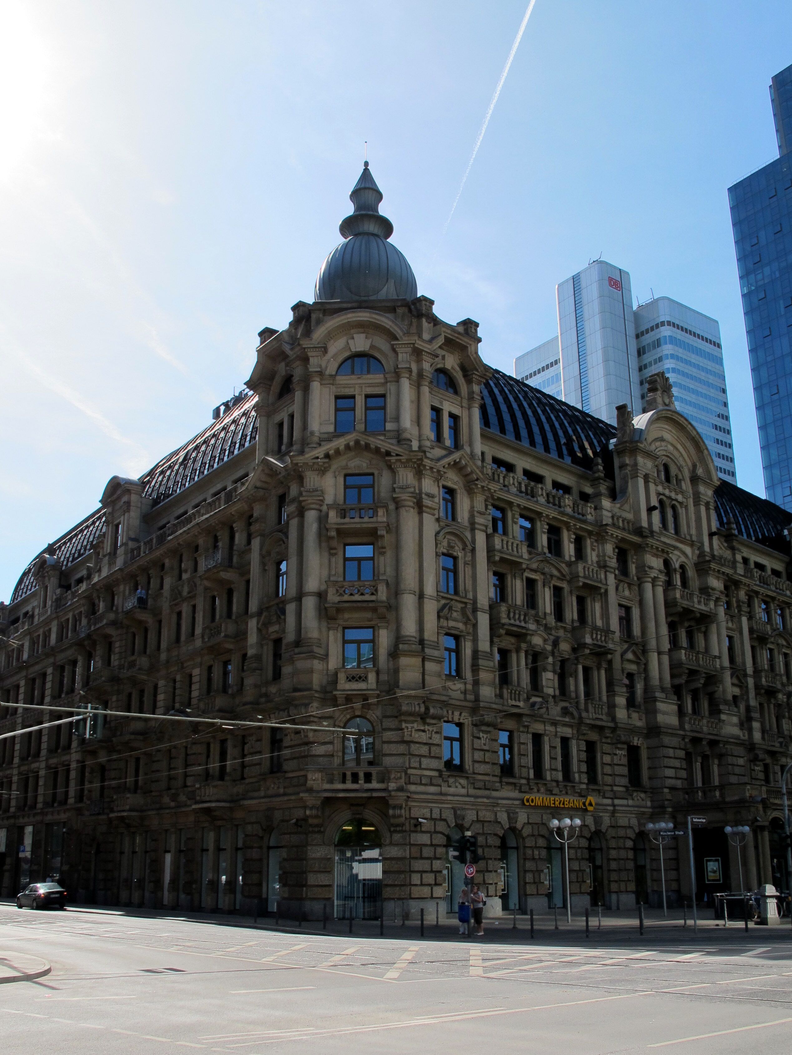 A historic building with ornate architecture, including a dome and columns, in an urban setting with modern skyscrapers in the background.