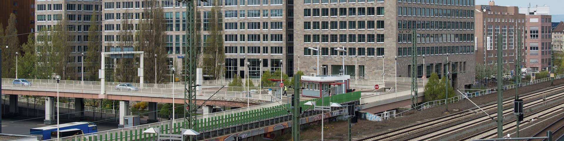 A tall, modern building with the "ibc" logo, surrounded by other buildings and a railway track.