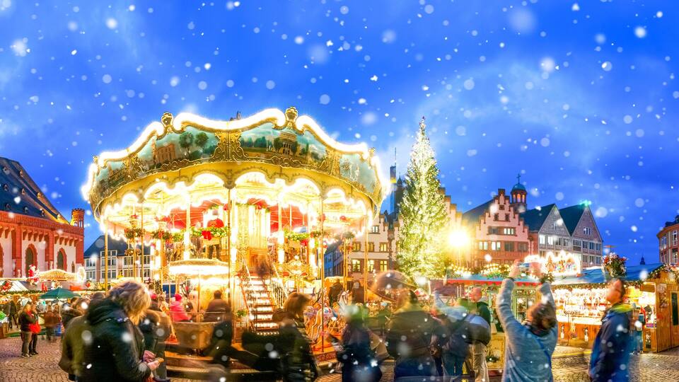 A festive market square with a carousel, a tall clock tower, and traditional buildings.