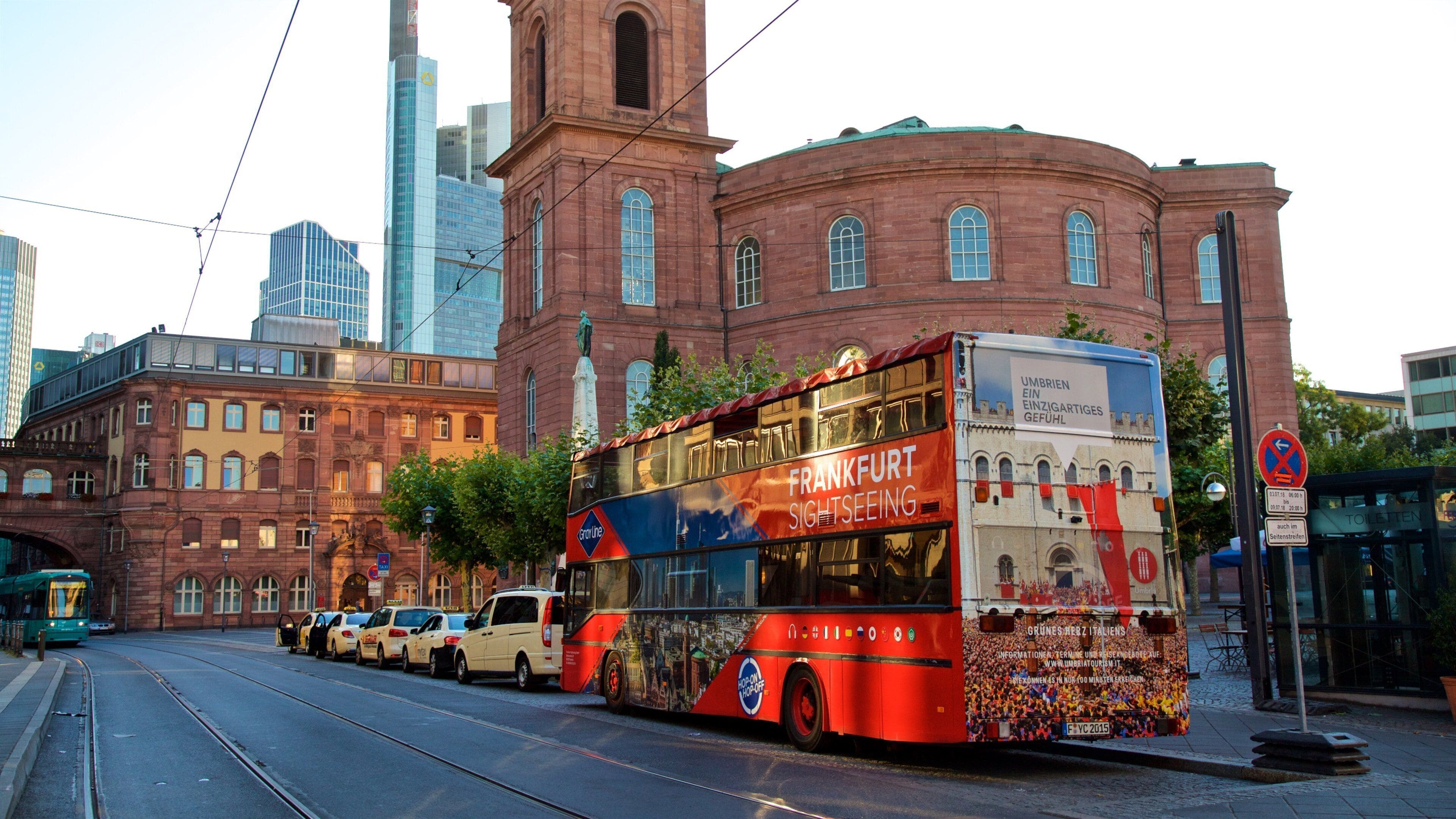 A red double-decker bus with "Frankfurt Sightseeing" on the side, parked on a street with tram tracks.