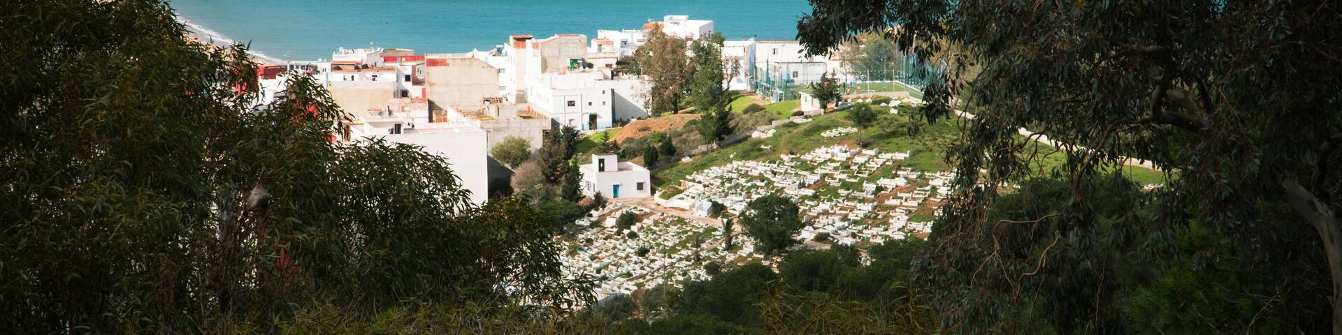 Panoramic view over M’diq, turquoise Mediterranean beach, hillside cemetery and white houses framed by dense vegetation, northern Morocco.