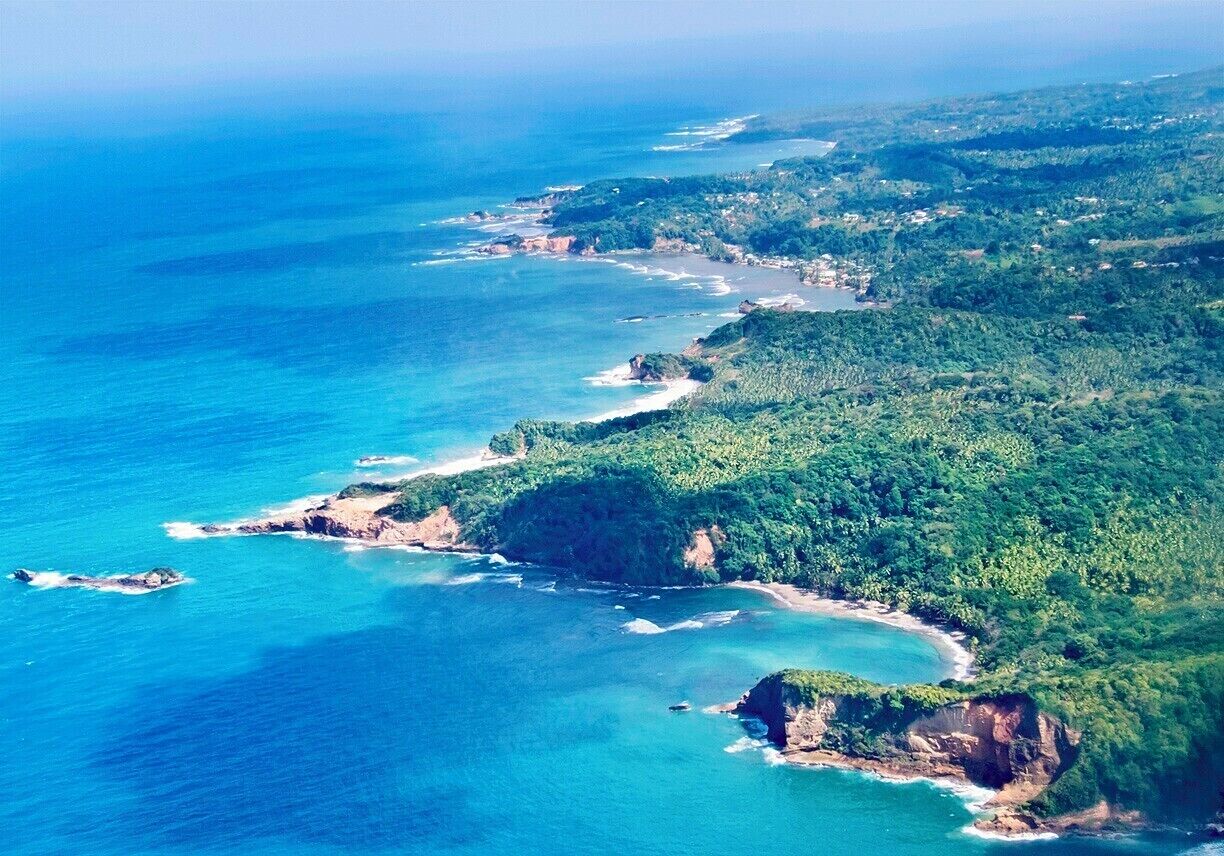 A coastal landscape with a clear blue sea, green hills, and a winding road along the coast.