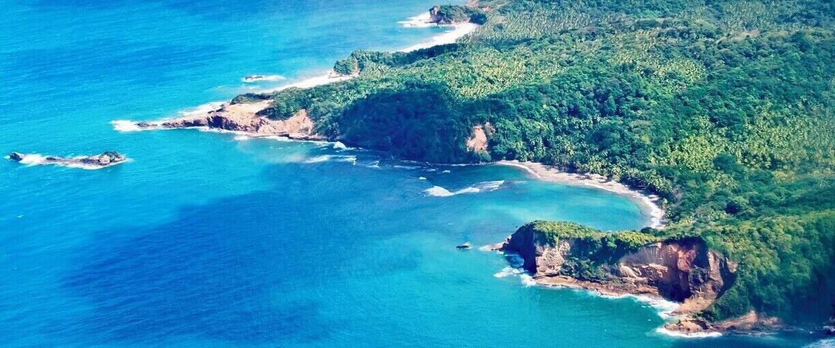 A coastal landscape with a clear blue sea, green hills, and a winding road along the coast.