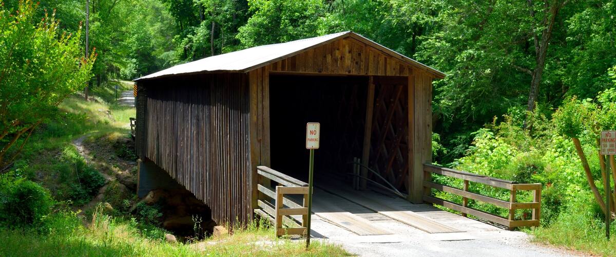 A wooden covered bridge with a 'No Parking' sign in front.