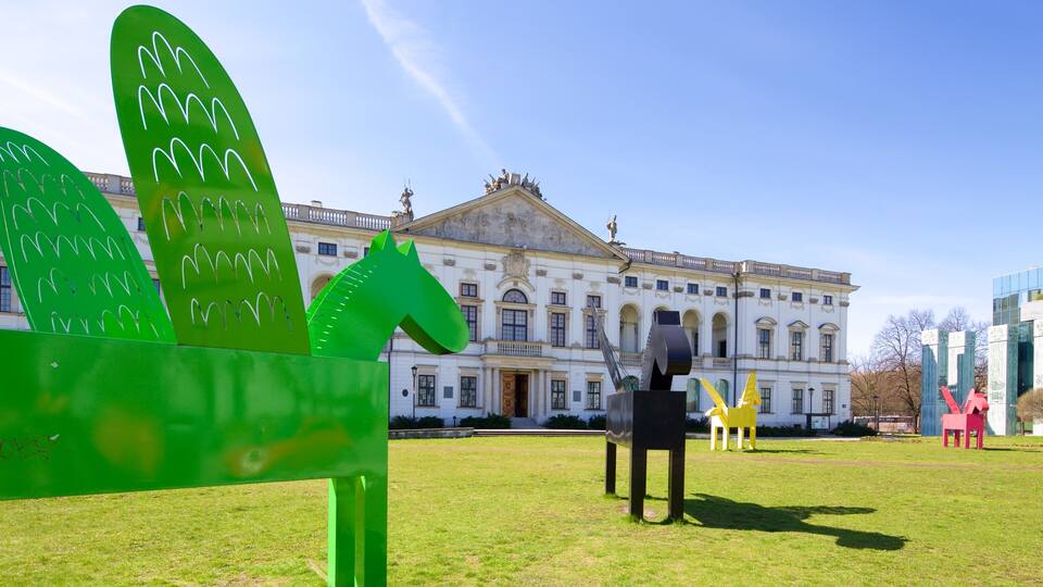 A large green sculpture in front of a classical building with a statue on top.