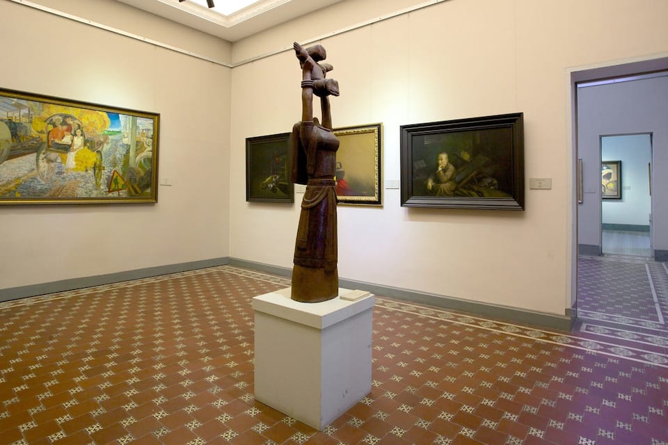 Ett konstgalleri med en skulptur i utställningen, omgiven av inramade målningar på väggarna.