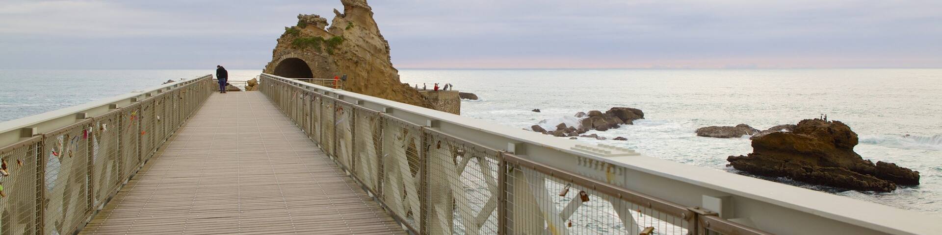 A wooden pier leading to a rocky coastline with a statue at the end.