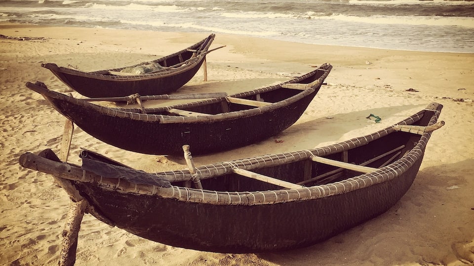 Drie traditionele boten op een zanderig strand, met de oceaan op de achtergrond.