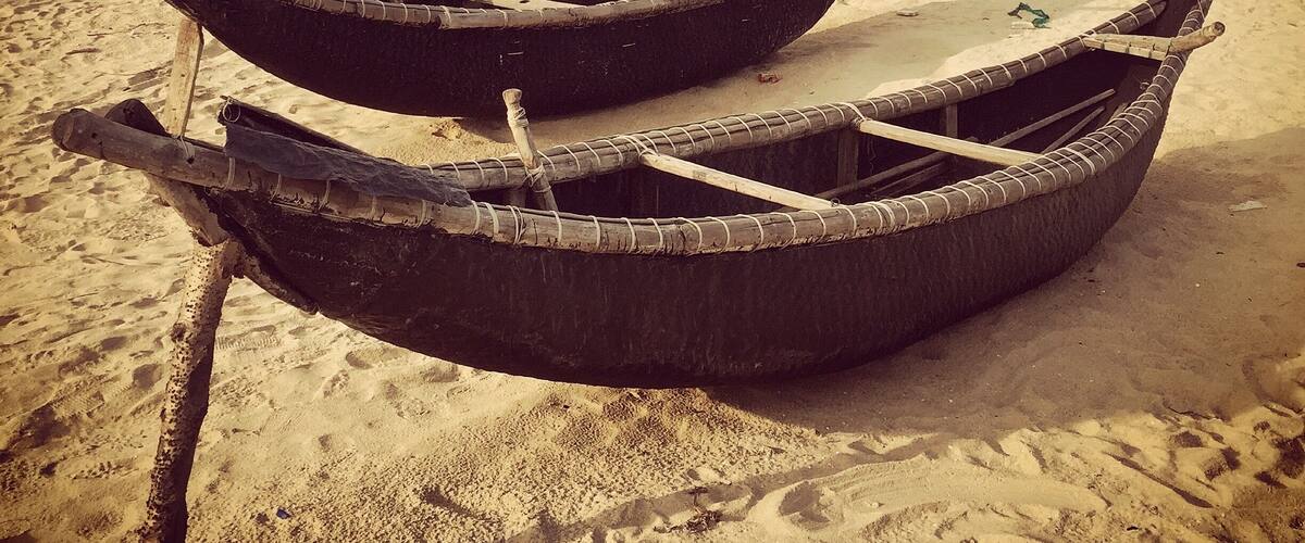 Three traditional boats on a sandy beach with the ocean in the background.