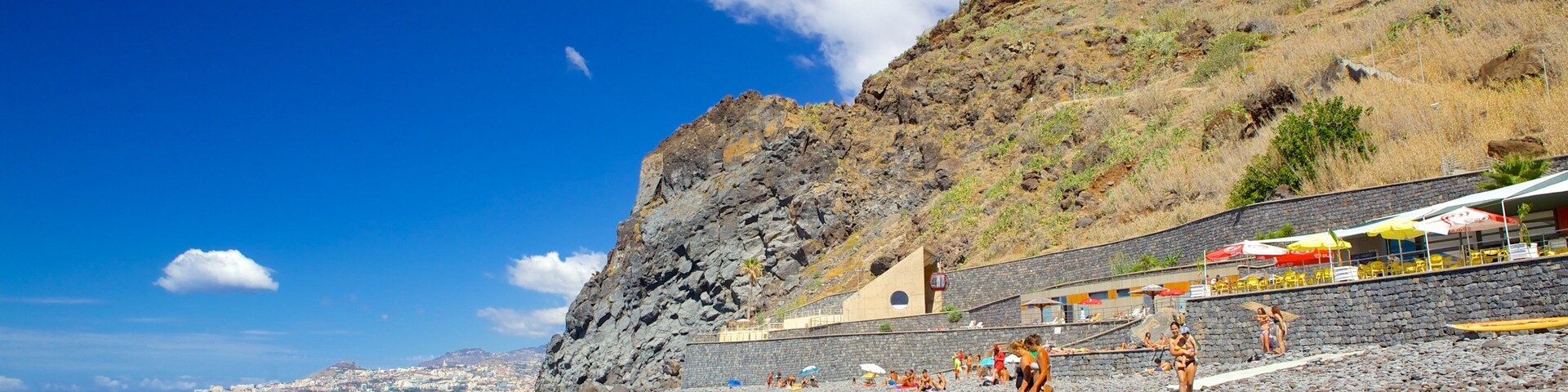 A rocky beach with a rocky cliff and a building with umbrellas.