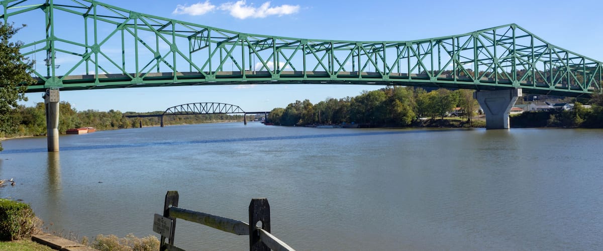 A green metal bridge over a river with a smaller bridge in the background.