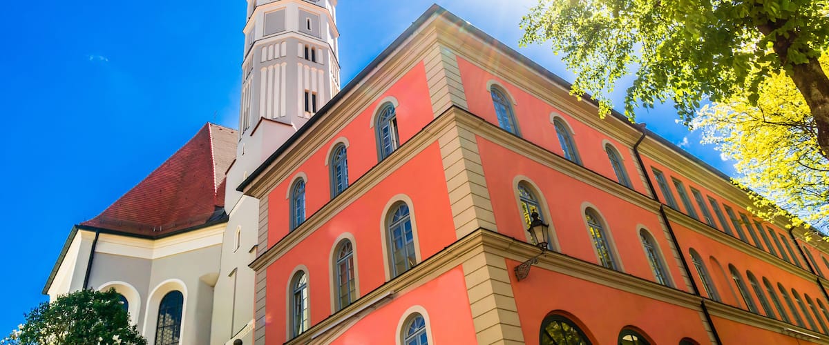 A church with a tall tower and a red building with arched windows.