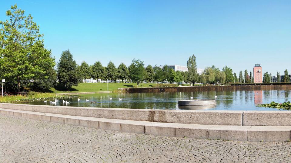 A park with a pond, trees, and a distant building.