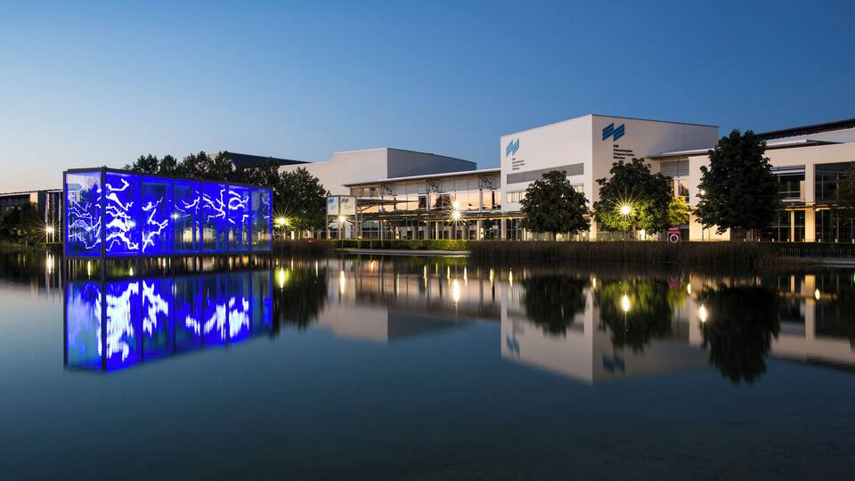 A modern building with a reflective water body in front.