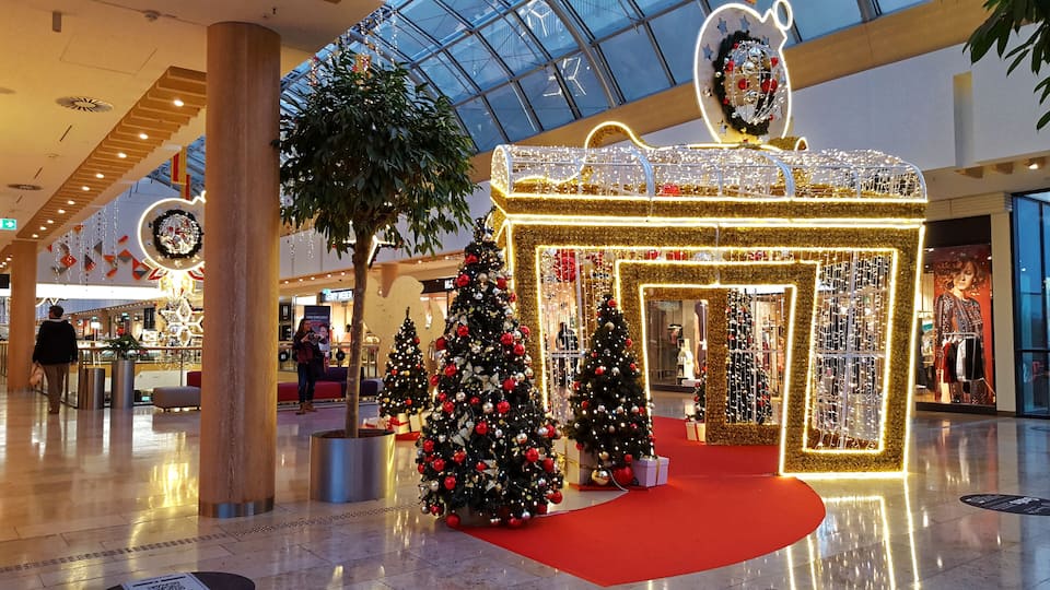 A shopping mall with Christmas decorations, including a large illuminated tree and a gift box structure.