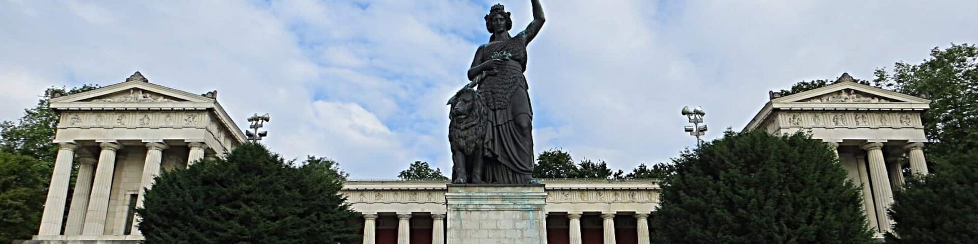 A neoclassical building with a statue of a woman raising her hand, flanked by two columns, and a staircase leading up to the entrance.