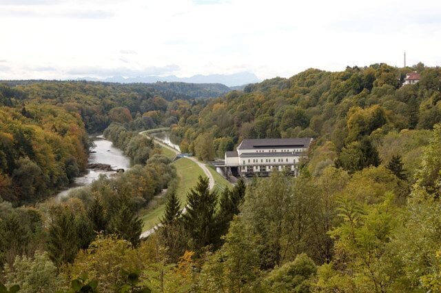 A river winding through a forested valley with a large building on a hill.