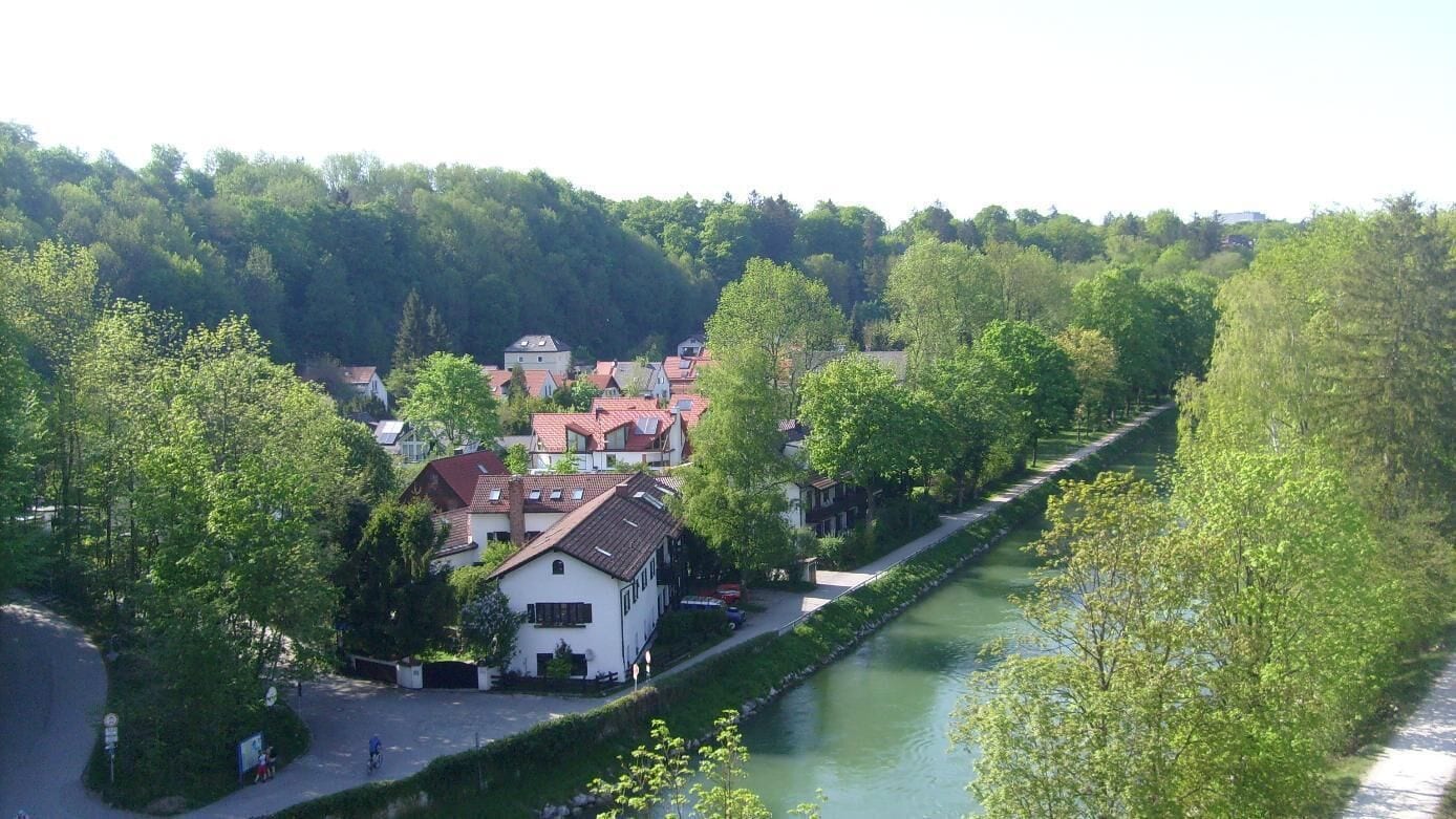 A riverside town with houses, a river, and a forested hill in the background.