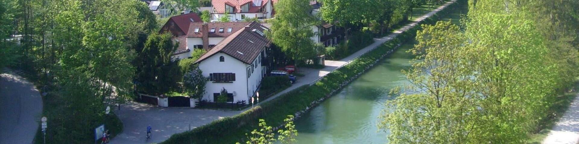 A riverside town with houses, a river, and a forested hill in the background.