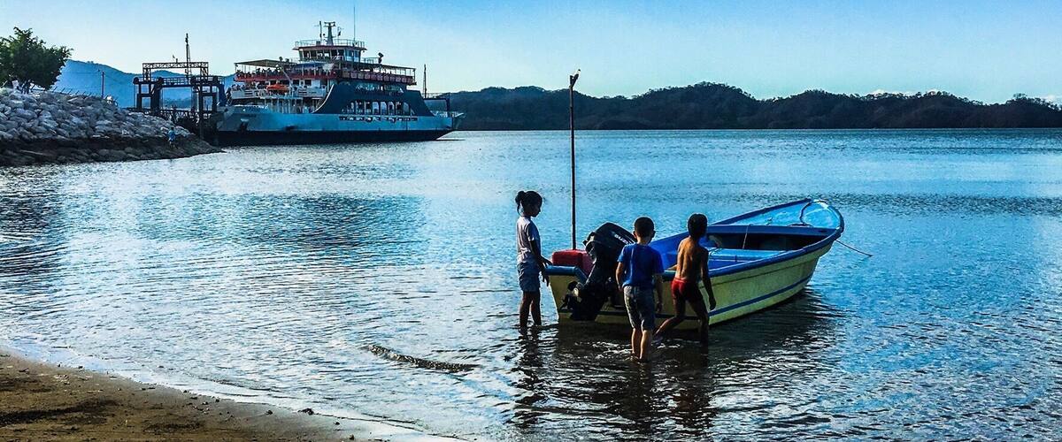 Costa Rican youth ready to take out their small boat with the big Paquera to Puntarenas ferry in the background #pacquera #puntarenas #ferry #costarica #nicoyapeninsula #boat #beach #ocean #puravida #lifeatexpedia