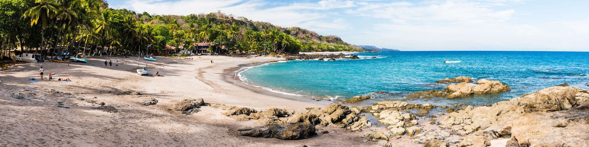 Uma praia tropical com águas turquesa cristalinas, costa rochosa e palmeiras.