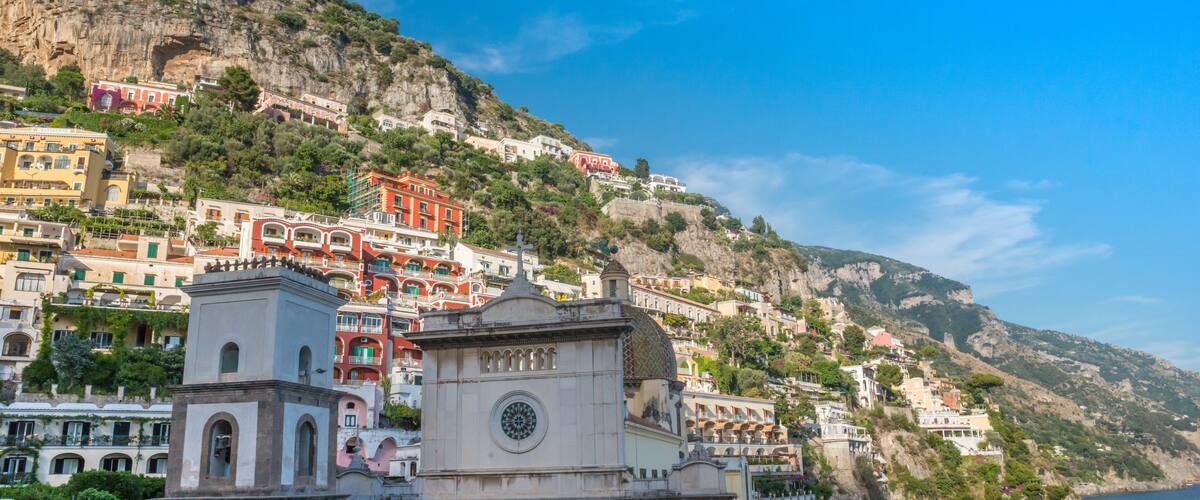 A coastal town with colorful buildings on a hillside, a prominent church with a dome, and a clear blue sky.