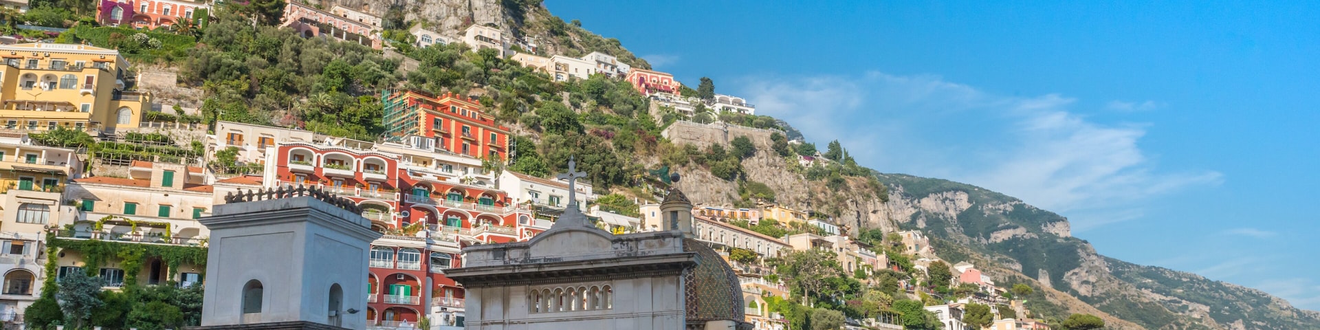 A coastal town with colorful buildings on a hillside, a prominent church with a dome, and a clear blue sky.