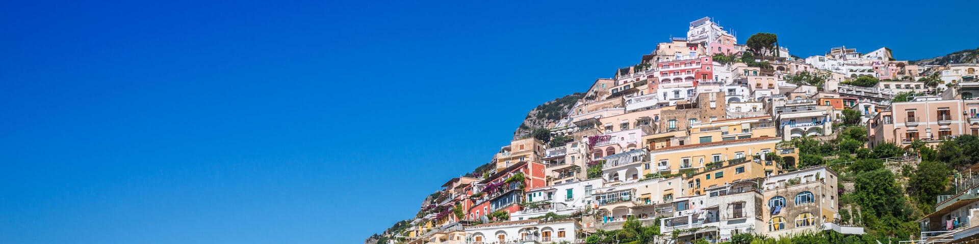 Un pueblo costero con edificios de colores en una ladera, barcos amarrados en el puerto y un cielo azul despejado.