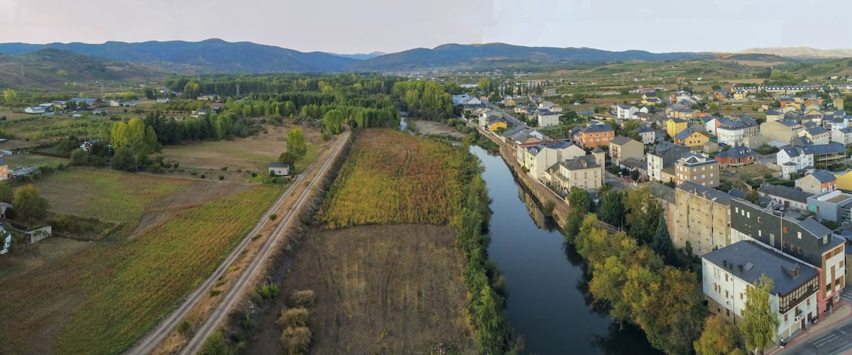 A river running through a town with surrounding fields and mountains in the background.