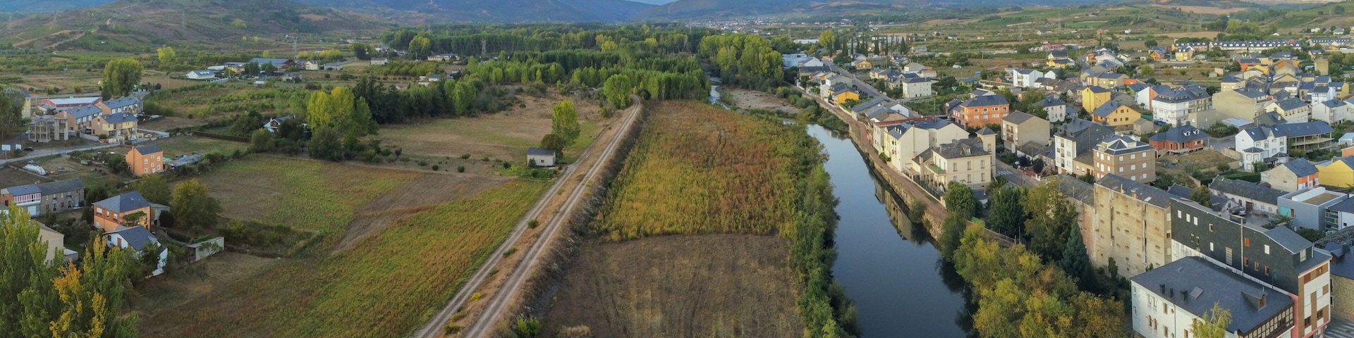 A river running through a town with surrounding fields and mountains in the background.